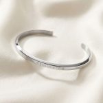 دستبند النگویی باز زنانه رنگ نقره‌ای با طراحی مینیمال و حکاکی نام برند دانیل ولینگتون (Daniel Wellington)