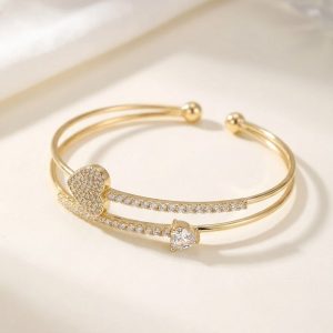 دستبند النگویی (بنگل) زنانه مجلسی رنگ طلایی با طراحی باز و دو لاین، تزئین شده با یک قلب تمام نگین و یک تک نگین قلبی شکل