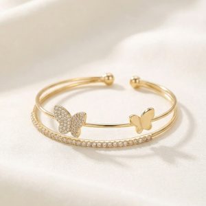 دستبند النگویی (بنگل) زنانه رنگ طلایی با طراحی باز دو لاین، دارای یک ردیف نگین ظریف و طرح دو پروانه درخشان و ساده