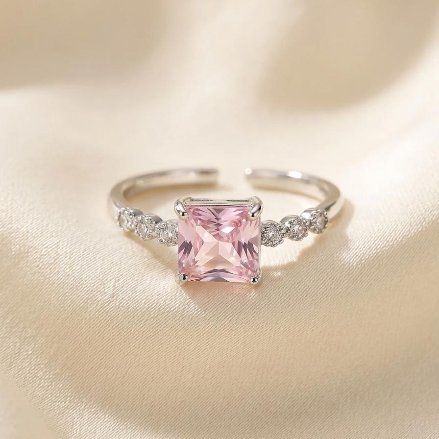 silver-pink-square-cz-ring-free-size انگشتر زنانه نقرهای رنگ فری سایز با یک نگین درشت مربعی شکل به رنگ صورتی روشن در مرکز و نگینهای ریز سفید روی رکاب.