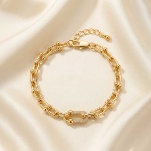 دستبند طلایی با طرح زنجیر U شکل (مدل تیفانی) و حلقه‌های مرکزی نگین‌دار، قرار گرفته روی پارچه حریر روشن