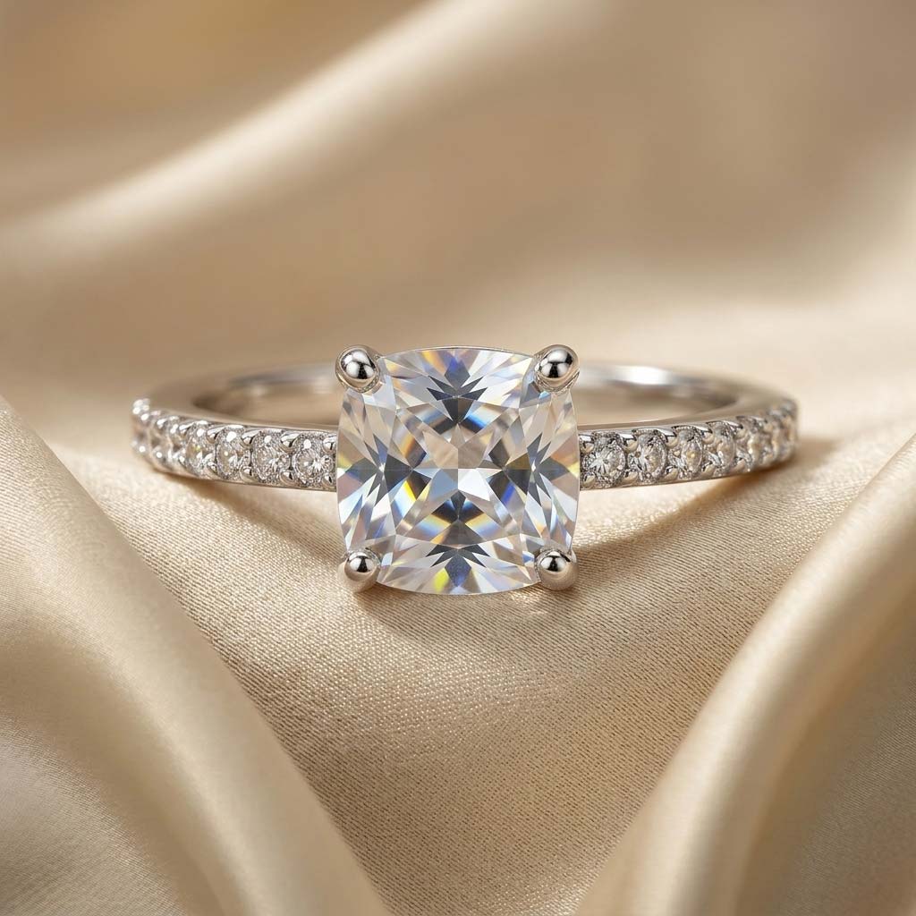 cushion-cut-solitaire-pave-band-free-size-engagement-ring انگشتر زنانه سولیتر با نگین درشت کوشن (مربع گوشه گرد) و رکاب نگیندار نقرهای روی پارچه ساتن