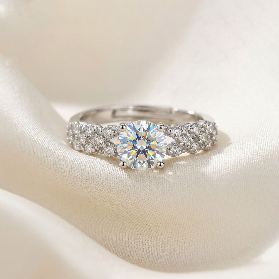 round-brilliant-infinity-twist-pave-band-free-size-engagement-ring.jpg انگشتر زنانه رنگ نقره ای مدل فری سایز با یک نگین گرد بزرگ در مرکز و بازوهای پیچ خورده (بافته) پوشیده از نگین های ریز روی پارچه حریر سفید