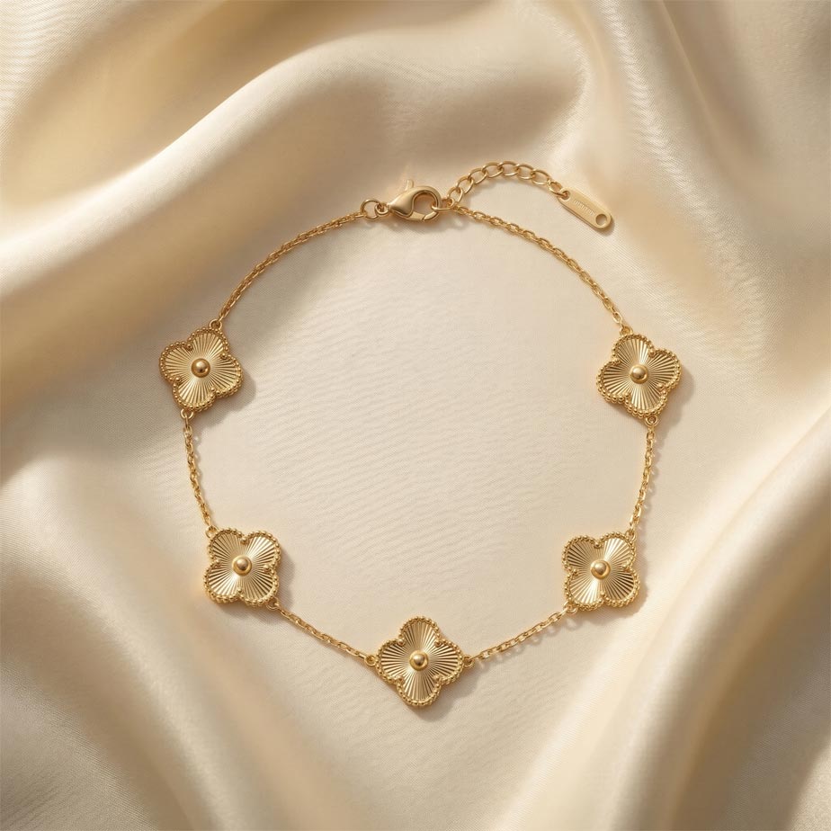 golden-bracelet-van-cleef-five-motif-sunburst دستبند طرح ون کلیف پنج گل طلایی رنگ قرار گرفته روی پارچه ساتن روشن با پلاکهایی به شکل شبدر چهار برگ که دارای شیارهای ظریف خورشیدی و یک گوی برجسته در مرکز هستند.